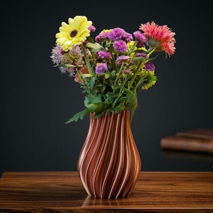 Könnte beinhalten: Eine braune, geriffelte Vase gefüllt mit einem lebendigen Blumenstrauß. Das Arrangement umfasst gelbe, lila und rosa Blüten mit grünem Laub. Die Vase steht auf einer Holzoberfläche vor einem dunklen Hintergrund.