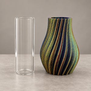 Op de afbeelding: Een heldere cilindrische glazen vaas naast een getextureerde, parelmoerachtige vaas met een spiraalvormig, geribbeld ontwerp dat verschuift tussen donkerblauwe, groene en bronzen tinten. Beide items staan rechtop en tonen hun vormen.