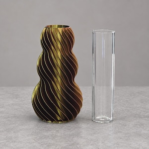 Puede incluir: Un jarrón de tres niveles en espiral con un acabado en bronce metálico y marrón oscuro, que presenta una silueta redondeada y ondulada. Junto a él hay un tubo de vidrio cilíndrico transparente diseñado para encajar en la abertura central.