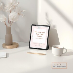 May include: A digital tablet showing the text "How to Create Your Own Course" with a pink floral design. A gold pen, a white coffee cup, and a vase with white flowers are on a white surface. A PDF download button is visible.