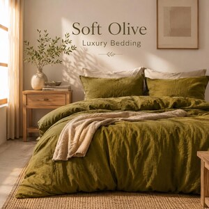 Op de afbeelding: Een bed met olijfgroene beddengoed, inclusief een dekbedovertrek en kussenslopen. Een beige deken is over het bed gedrapeerd. De tekst "Soft Olive Luxury Bedding" staat boven het bed. Een houten nachtkastje en een vaas met groen zijn zichtbaar.