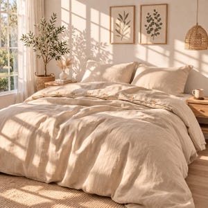 May include: A beige linen duvet cover set with matching pillowcases on a bed. The duvet cover has wooden button closures. The bedroom is decorated in neutral tones with framed botanical prints and a woven pendant light.