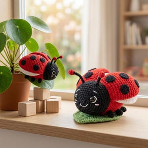 Puede incluir: Dos mariquitas hechas a mano con ganchillo. Las mariquitas tienen cuerpos rojos con lunares negros, cabezas negras y detalles blancos. Una mariquita está sobre una hoja verde, la otra sobre una hoja. Las mariquitas están sobre una superficie de madera cerca de una planta.