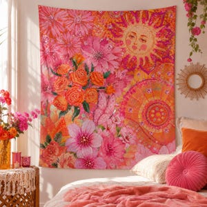 Puede incluir: Un tapiz de pared rectangular con un estampado vibrante de flores rosas y naranjas, un sol estilizado con rostro humano y una mariposa. El diseño incorpora varios patrones florales, motivos circulares y degradados de colores cálidos.