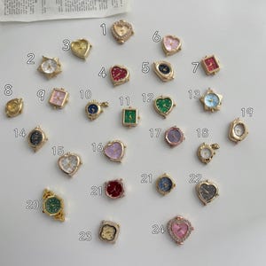 May include: A collection of twenty-four small gold-tone watch faces in various shapes including hearts, stars, rectangles, and circles, each labelled with a number from 1 to 24. The watch faces feature diverse dial colours like red, green, blue, pink, and white.