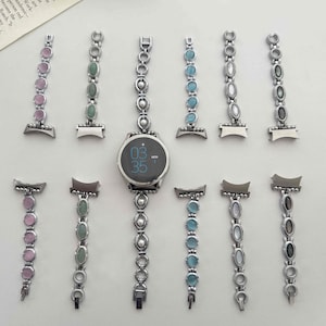 May include: A silver-toned smartwatch with a round digital display showing 03:35, surrounded by ten interchangeable watch bands. Each band features a series of oval-shaped cabochon stones in various colors including pink, green, blue, white, and gray.