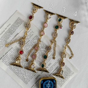 Op de afbeelding: Gouden horlogebandjes met decoratieve bedels en edelstenen. Elke band heeft een andere opstelling van juwelen, waaronder roze, groene en rode stenen, en wordt getoond op een vintage receptenpagina.