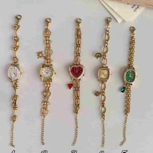 May include: Five gold-tone wristwatches with decorative link chains. Watch 1 has a white face, 2 has a white face with charms, 3 has a red heart-shaped face with a heart charm, 4 has a square face with charms, and 5 has a green face with a teardrop charm.