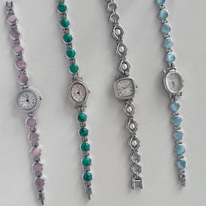 May include: Four silver-tone wristwatches with decorative link bracelets. The first has pink cabochon stones, the second features green turquoise-style stones, the third includes white pearl-like beads, and the fourth displays light blue cabochon stones.