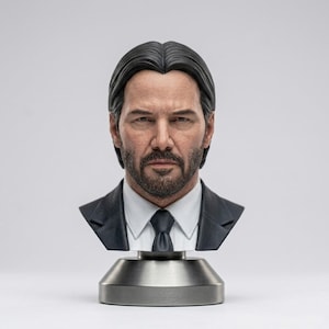 May include: A detailed bust of a man with dark hair and a beard, wearing a suit and tie. The sculpture is mounted on a silver-colored base. The bust is a realistic representation of a person.