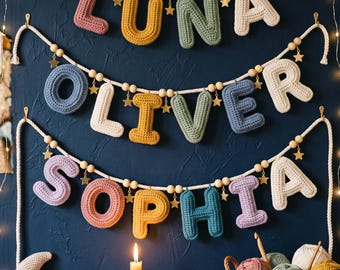 May include: Three horizontal garlands featuring crocheted letters spelling LUNA, OLIVER, and SOPHIA. The letters are in various colors including pink, yellow, green, blue, and cream, accented with wooden beads and small gold star charms on white rope.