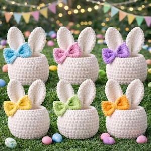 Puede incluir: Seis cestas de conejito de ganchillo de color crema con orejas erguidas y lazos coloridos. Los lazos son azules, rosas, morados, amarillos, verdes y naranjas. Las cestas están sobre hierba verde con huevos de Pascua coloridos.