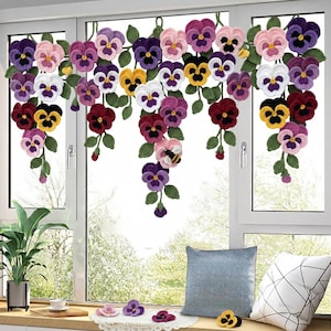 May include: A crocheted window valance with vibrant pansies in purple, pink, yellow, and white. The flowers are attached to green vines, creating a decorative floral display. A small bee is also included in the design.