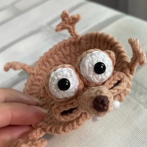 May include: A handmade crochet creature with large white eyes, black pupils, and a brown nose. The crochet animal has a light brown body and is likely a bookmark or decorative item.
