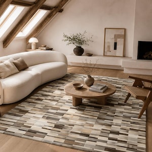 May include: A rectangular area rug featuring a geometric pattern of varied rectangular tiles in shades of cream, beige, grey, and dark brown. The rug has a flat, smooth texture and covers a large portion of the light-coloured wooden floor.
