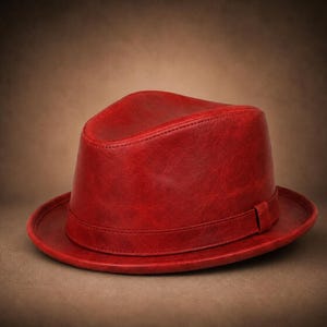 May include: A vibrant red fedora hat featuring a smooth, leather-like texture with a matching red band encircling the base of the crown. The hat has a structured shape with a pinched top and a wide, flat brim, showcasing consistent stitching.