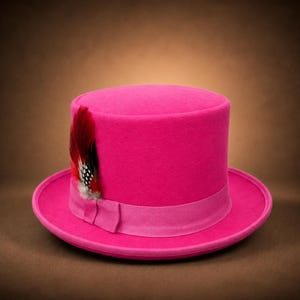 May include: A vibrant hot pink top hat featuring a matching pink grosgrain ribbon band around the base. A decorative feather accent in shades of red, black, and white with small polka dot patterns is tucked into the side of the ribbon band.