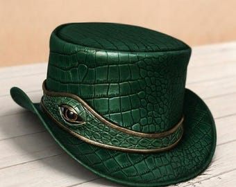 May include: A dark green top hat featuring a textured crocodile skin pattern. The hat is encircled by a matching green band with a metallic gold trim and a central decorative eye element with a brown iris and a black pupil centered on the front.