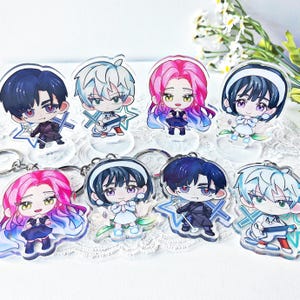 Op de afbeelding: Een verzameling van acht acryl sleutelhangers met anime-stijl karakters. Elke sleutelhanger toont een ander karakter met unieke haarkleuren, outfits en poses. De sleutelhangers staan op transparante standaards en hebben zilveren sleutelringen.