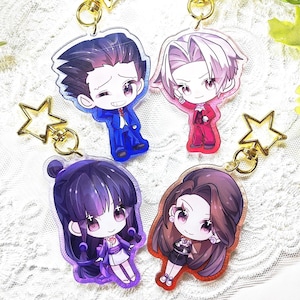 May include: Four acrylic keychains featuring chibi-style anime characters. Two keychains have gold star-shaped clasps, and two have gold circular clasps. The characters include a person in a blue suit, a person in a red suit, a person in purple robes, and a person in a dark outfit with long hair.
