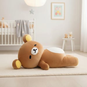 Puede incluir: Un gran oso de peluche marr&oacute;n con detalles amarillos en las orejas est&aacute; tumbado sobre una alfombra color crema. El oso tiene una mancha blanca en la espalda y una peque&ntilde;a nariz y boca negras. El peluche est&aacute; en un cuarto de ni&ntilde;os.