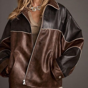 Könnte beinhalten: Braune und schwarze Kunstlederjacke mit Reißverschluss vorne. Die Jacke hat einen Kragen und weiße Paspeln entlang der Nähte. Die Jacke hat eine lockere Passform und ein klassisches Design.