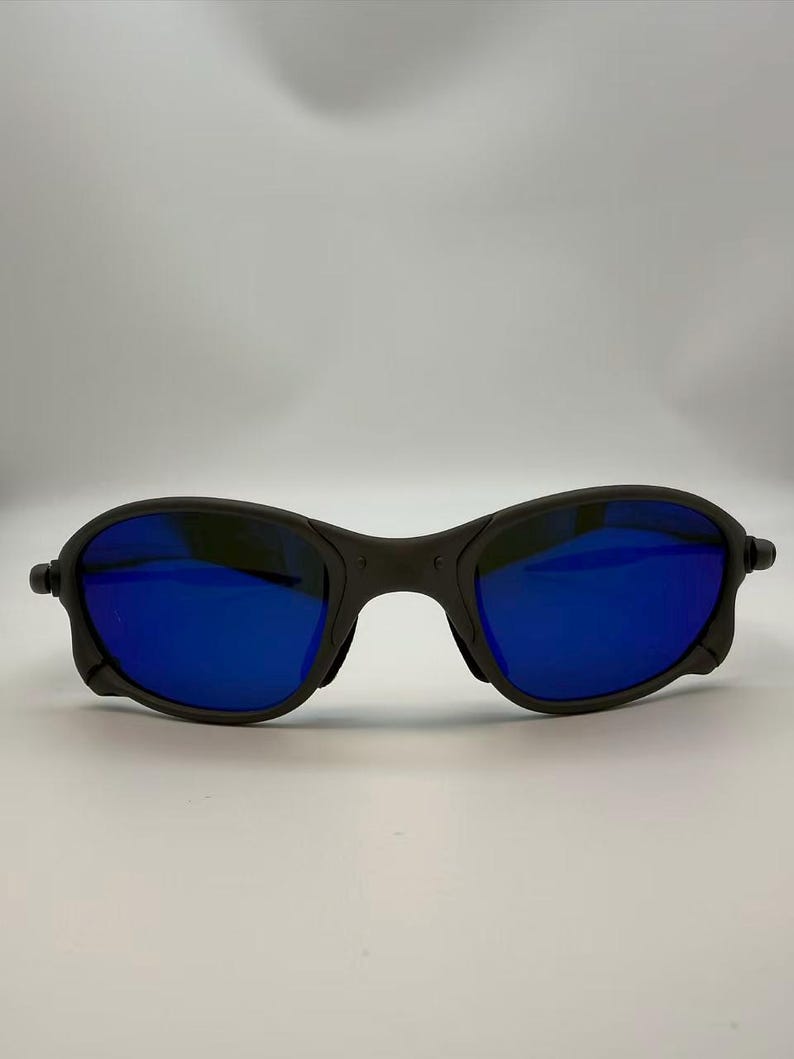 Puede incluir: Gafas de sol negras con lentes de espejo azules. Las gafas tienen una montura redondeada y un dise&ntilde;o deportivo. Las lentes reflejan un color azul brillante, y la montura es de color negro mate. Las gafas est&aacute;n dise&ntilde;adas para actividades al aire libre.