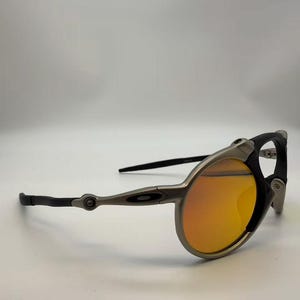 May include: Sport sunglasses with a silver frame, black accents, and orange lenses. The sunglasses have a unique design with a curved frame and sleek temples. The lenses are a vibrant orange color, providing a stylish look.
