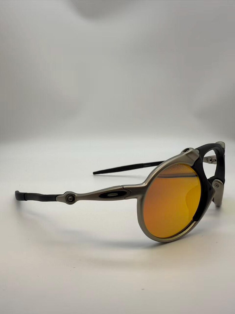 May include: Sport sunglasses with a silver frame, black accents, and orange lenses. The sunglasses have a unique design with a curved frame and sleek temples. The lenses are a vibrant orange color, providing a stylish look.