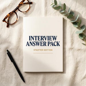 May include: A cream-colored book titled "INTERVIEW ANSWER PACK STARTER EDITION" with navy blue text. Tortoiseshell glasses and a black pen are on the left. A sprig of green leaves is on the right. The items are on a textured, off-white surface.