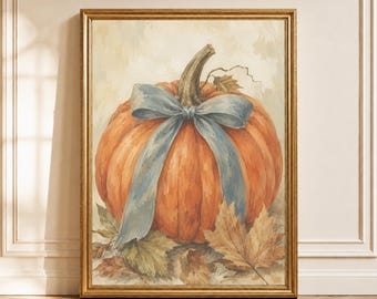 May include: A framed wall art print featuring a large orange pumpkin with a prominent light blue ribbon tied around its stem. The pumpkin rests on a bed of dried autumn leaves against a neutral, textured background, all encased in a gold frame.
