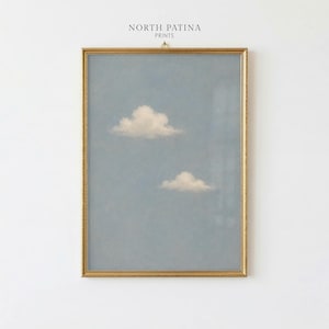 May include: A vertical rectangular wall art print in a thin gold frame featuring a light blue sky with two soft white clouds. The text NORTH PATINA PRINTS is centred above the frame. The artwork displays a calm, clear atmosphere with muted tones.