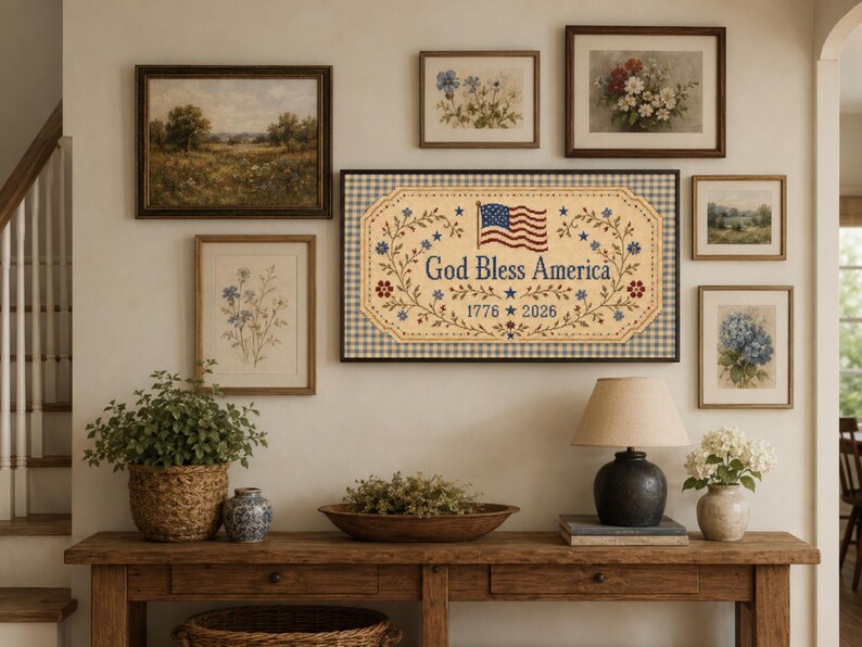 Pu&ograve; includere: Una targa da parete rettangolare con sfondo beige e bordo a quadretti vichy blu e bianchi. Il testo recita God Bless America con gli anni 1776 e 2026. Include una grafica della bandiera americana e motivi decorativi a tralci floreali.