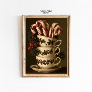 Pode incluir: Uma impressão artística emoldurada com a etiqueta NORTH PATINA PRINTS apresentando uma pilha de três xícaras de chá cor de creme decoradas com folhas de azevinho e bagas vermelhas. A xícara superior contém bengalas doces listradas de vermelho e branco.