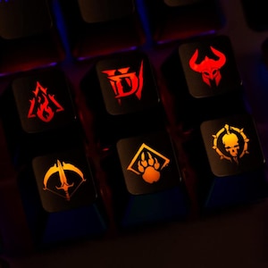 Puede incluir: Un juego de seis teclas mecánicas negras para teclado con iconos de juego retroiluminados en naranja y rojo. Los diseños incluyen una letra D estilizada, un casco con cuernos, un triángulo en llamas, un arco con flecha, una huella y una calavera.