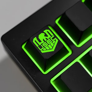 Op de afbeelding: Close-up van een zwart mechanisch toetsenbord met groene achtergrondverlichting. De toetsdoppen zijn zwart, met een groen logo en de tekst "USEC". Het toetsenbord heeft een modern, strak design.