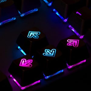 May include: Black mechanical keyboard keycaps featuring translucent arrow icons that glow with vibrant blue and purple LED backlighting. The keys are arranged in a directional cluster, with each cap displaying a distinct arrow symbol on its surface.