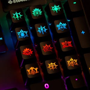 May include: A black computer keyboard featuring custom keycaps with illuminated, multi-coloured fantasy-style symbols. The keys display various glowing icons in shades of red, orange, blue, and green, alongside standard keys labelled M3, M6, and ENTER.