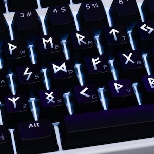 May include: A black computer keyboard with backlit keys featuring white runic symbols and corresponding Latin alphabet letters printed on each keycap. The keys are arranged in a standard layout with a white base visible beneath the black keys.