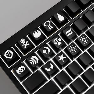 May include: Close-up of a black mechanical keyboard with custom keycaps. The keycaps feature white symbols and icons, including a skull and crossbones, a star, and other abstract designs. The keyboard has white LED backlighting.
