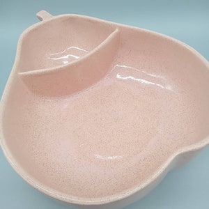 May include: A pink ceramic serving dish shaped like a pear with a divided section. The dish has a speckled finish.