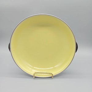 May include: A yellow enamel cast iron skillet with black handles. The skillet is on a gold stand.