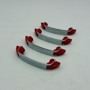 May include: Four vintage cabinet handles. Each handle has a curved, silver-colored metal bar with red end pieces. The handles are arranged on a white surface, showcasing their design and color contrast.