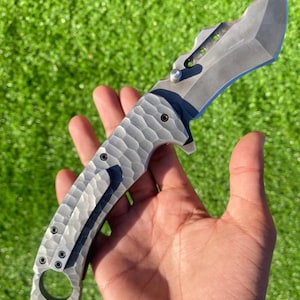 May include: A gray folding knife with a textured handle and a curved blade. The knife has a pocket clip and a hole at the base of the handle. The blade is approximately 4 inches long.