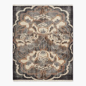 May include: A rectangular rug with a large floral pattern. The rug has a dark grey background with a repeating pattern of stylized flowers in cream, brown, and grey. The edges have a fringed border.