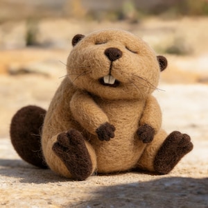 Puede incluir: Una figura de castor de peluche hecha a mano, con un cuerpo marrón claro, una cola marrón oscuro y pequeñas patas marrones oscuras. El castor tiene los ojos cerrados, una pequeña nariz y dos dientes frontales prominentes. La figura está sentada.