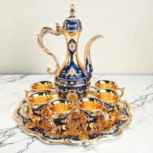 Könnte beinhalten: Ein verziertes Teeservice mit einer goldfarbenen Teekanne und sechs passenden Tassen, alle mit aufwendigen blauen und goldenen Details. Das Set enthält ein dekoratives Tablett, ideal zum Servieren von Tee oder Kaffee. Das Design ist elegant.