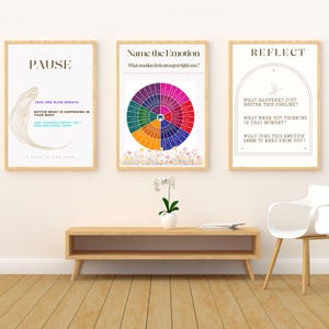Puede incluir: Tres impresiones artísticas enmarcadas con marcos de madera. Las impresiones presentan texto y gráficos relacionados con el bienestar emocional. Una impresión dice "PAUSE", otra "Name the Emotion" y la tercera "REFLECT". Las impresiones se muestran encima de una consola de madera.
