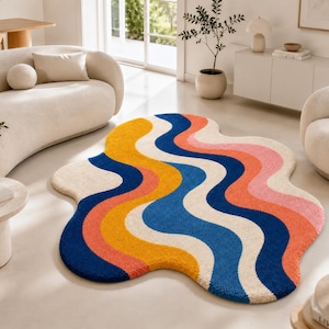 May include: An irregular, organic-shaped area rug featuring a wavy, multi-coloured pattern. The design consists of repeating, flowing bands in vibrant shades of mustard yellow, deep navy blue, coral orange, and soft cream, creating a bold visual.