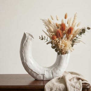 Könnte beinhalten: Ein Set aus drei Keramikbechern mit gesprenkelter, matter Oberfläche. Die Becher sind in Creme-, Hellgrau- und Dunkelgrautönen gehalten. Jeder Becher hat ein schlichtes, minimalistisches Design, ideal für Kaffee oder Tee.